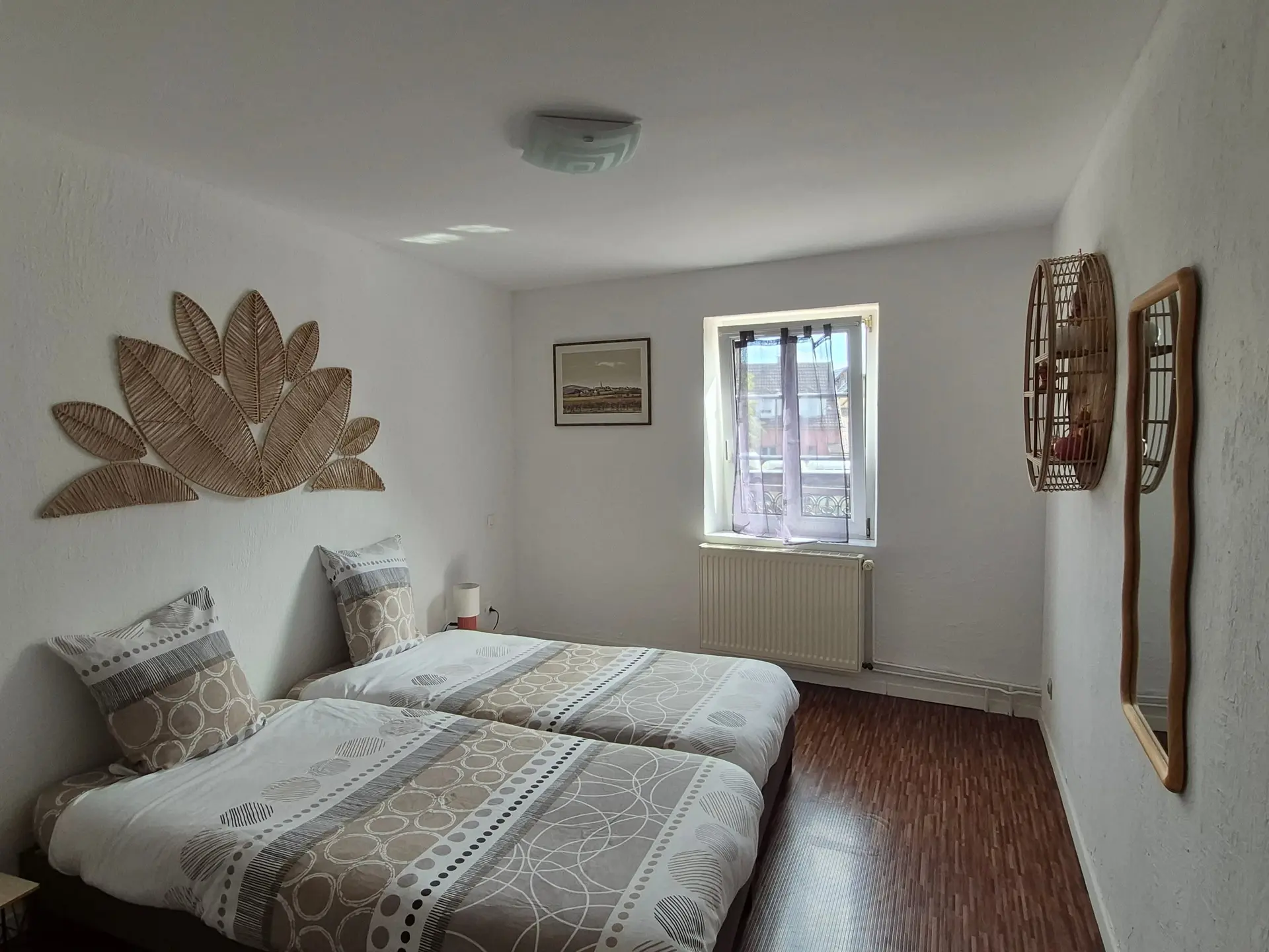 Chambre avec deux lits simples réunis en lit double, parure beige et tête de lit décorative.