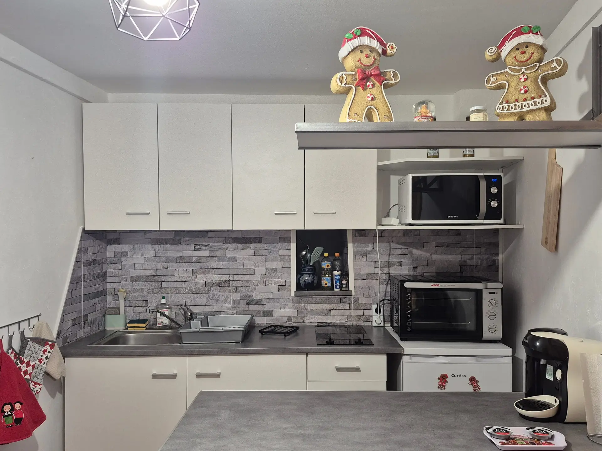 Cuisine équipée blanche avec plaque, four, micro-ondes et plan de travail en îlot.