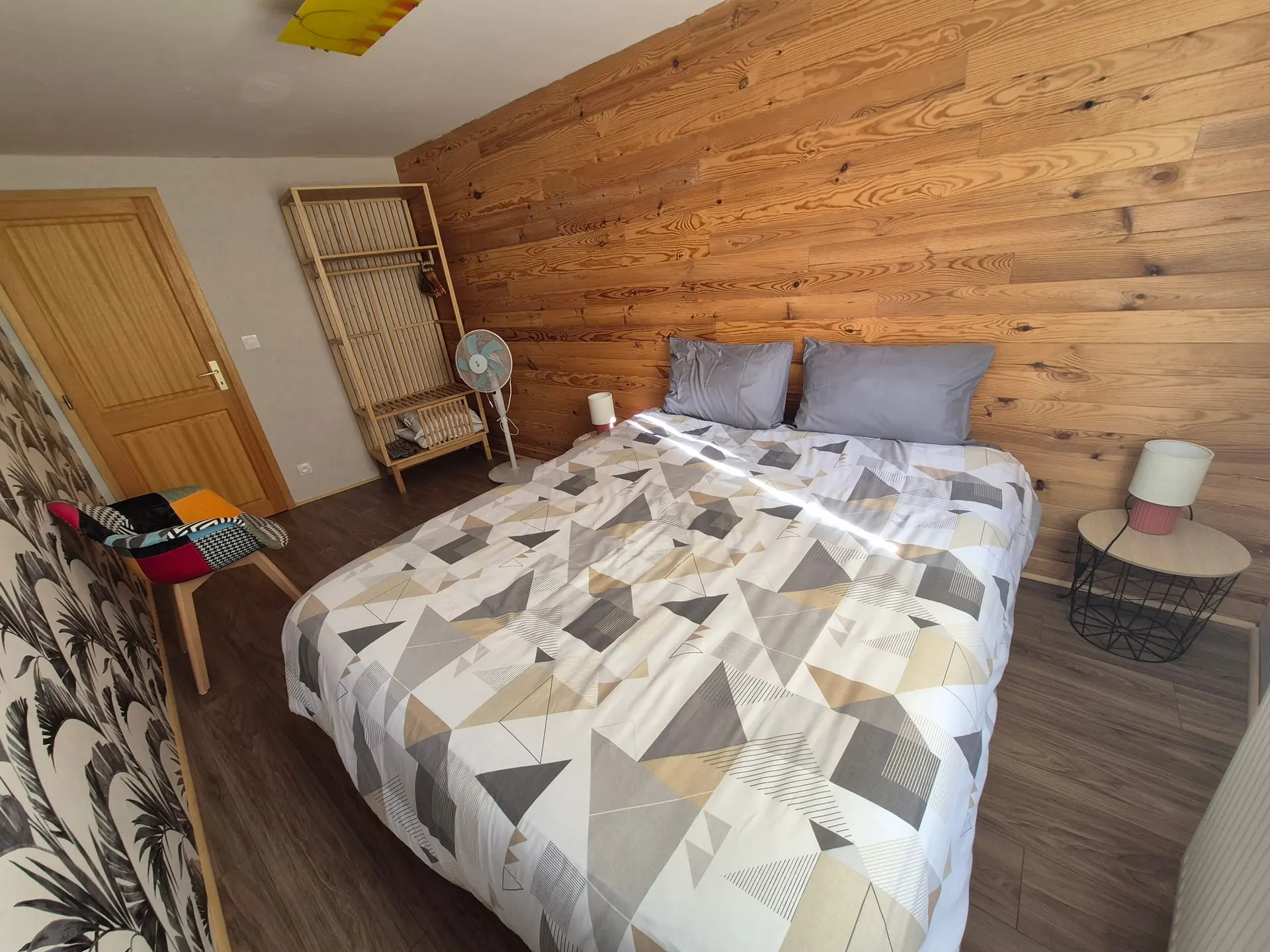 Chambre avec un lit double devant un mur lambrissé de bois clair, parure à motifs géométriques.