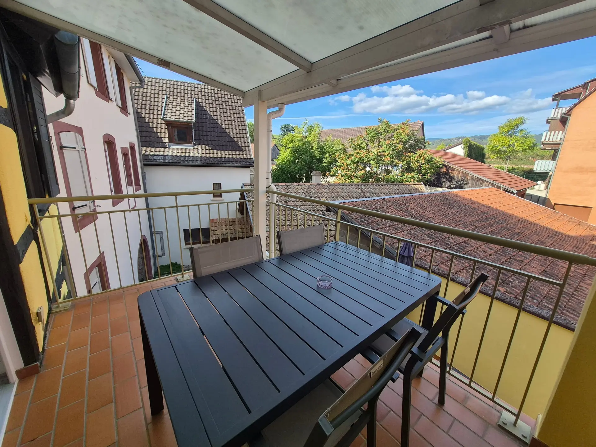 Terrasse couverte avec table et chaises, ouverte sur les toits du village.