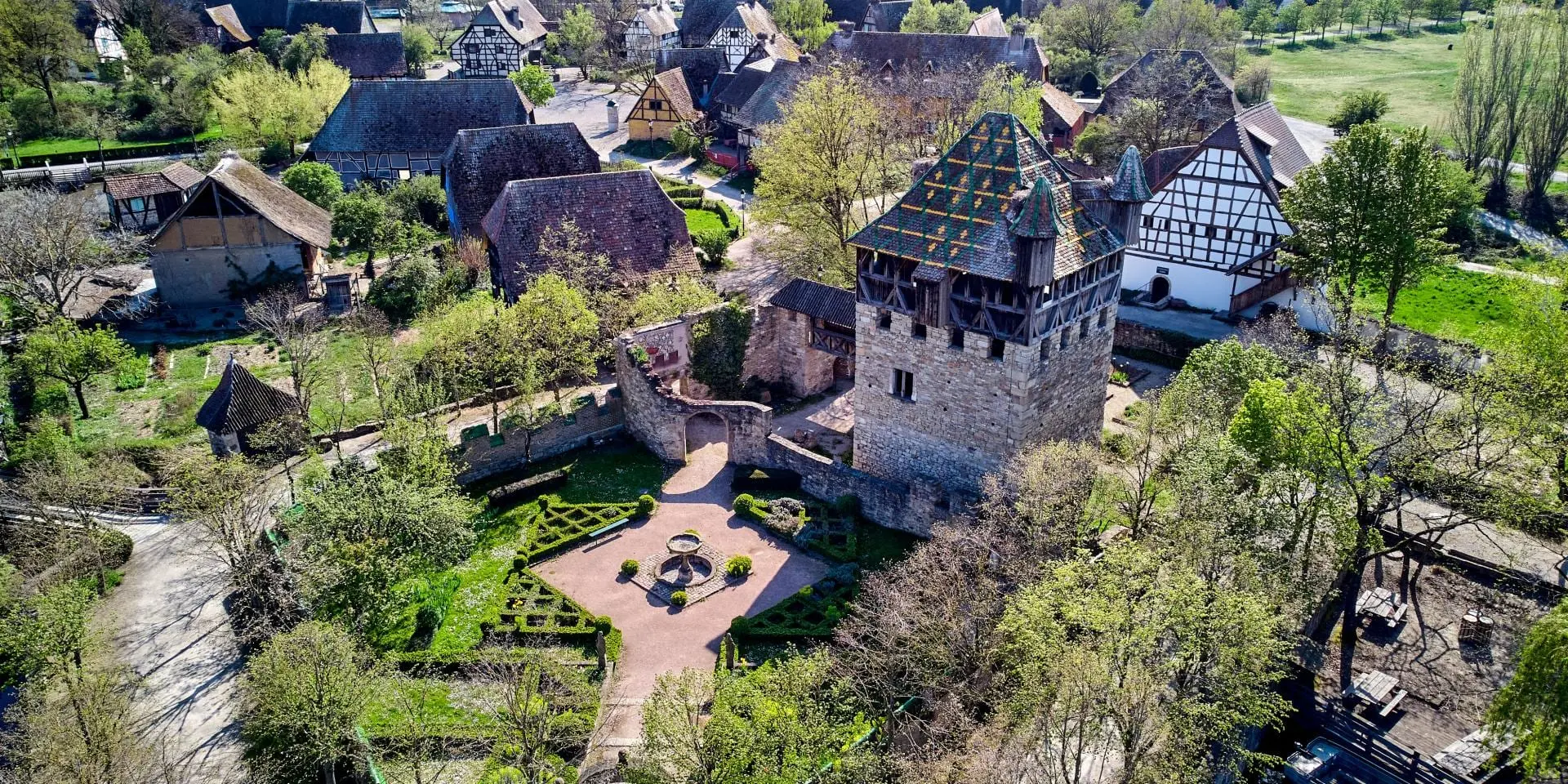 Vue aérienne de l'Écomusée d'Alsace : sa tour fortifiée, son jardin à la française et ses maisons à colombages.