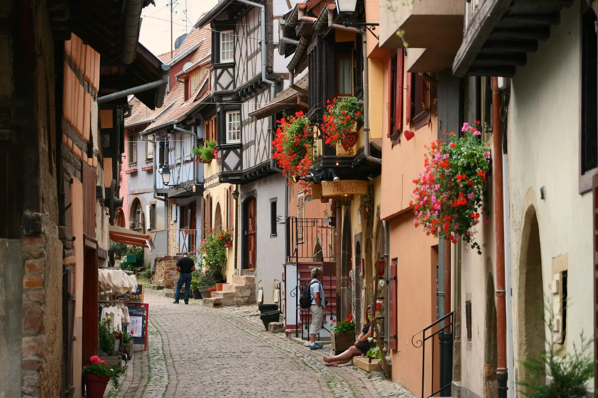 Une ruelle pavée d'Eguisheim, entre maisons à colombages et balcons fleuris de géraniums.