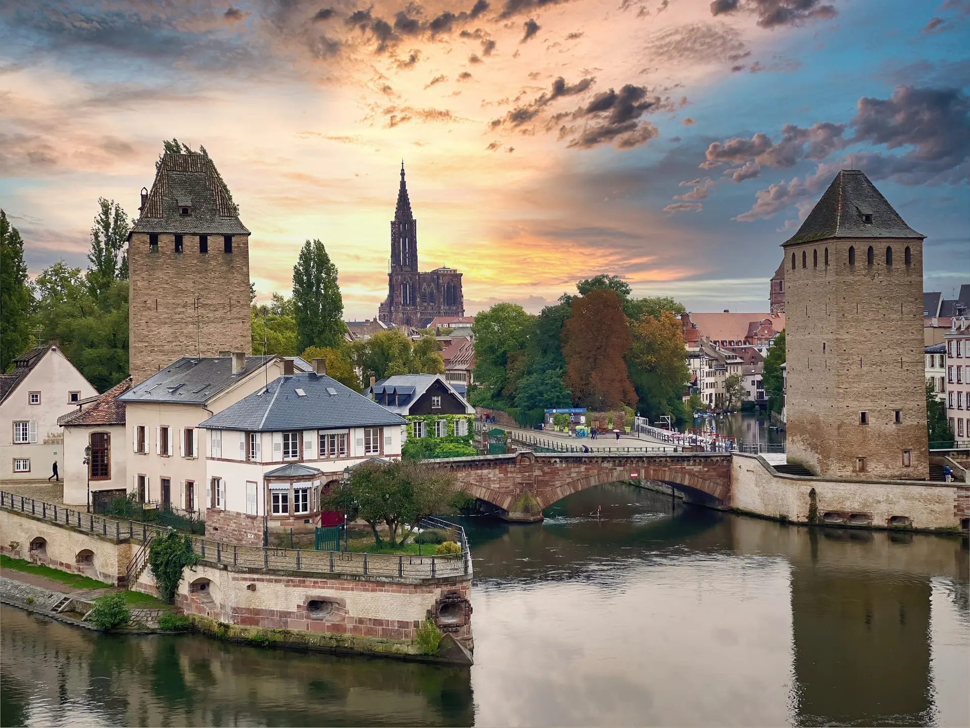 Les Ponts couverts de Strasbourg et leurs tours médiévales au coucher du soleil, avec la cathédrale à l'horizon.